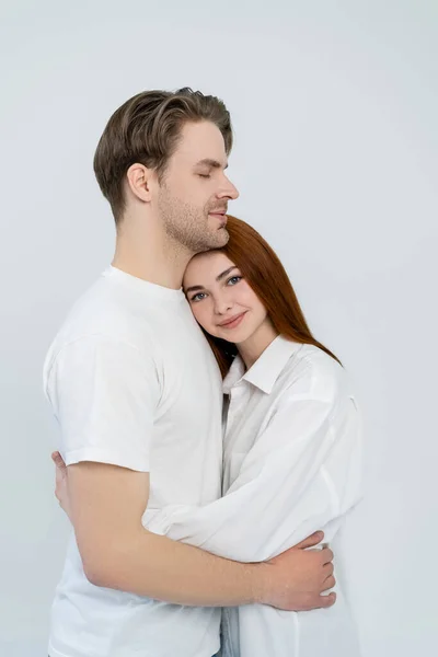 Mujer pelirroja positiva abrazando novio aislado en blanco - foto de stock