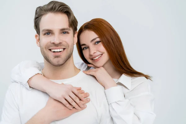 Sorridente donna dai capelli rossi abbracciare fidanzato isolato su bianco — Foto stock