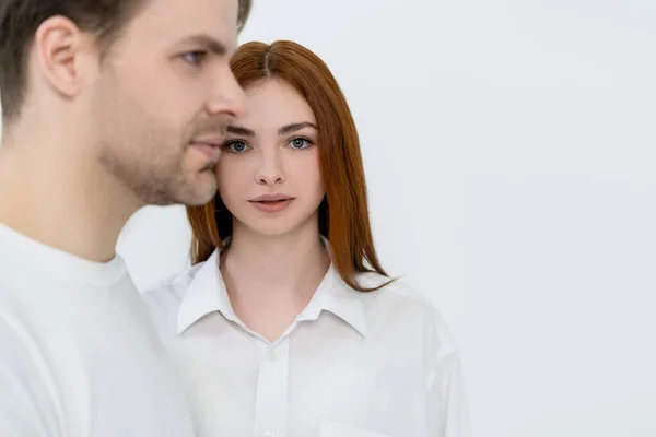 Young woman looking at camera near blurred boyfriend isolated on white — Stock Photo
