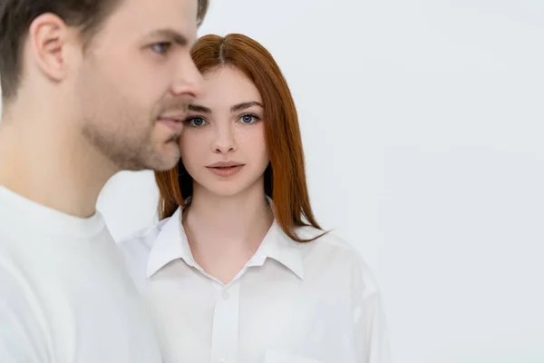 Young woman looking at camera near blurred boyfriend isolated on white — Stock Photo