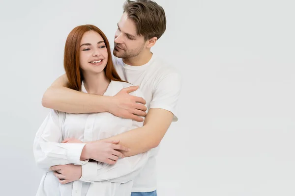Чоловік обіймає усміхнену дівчину в сорочці ізольовано на білому — стокове фото