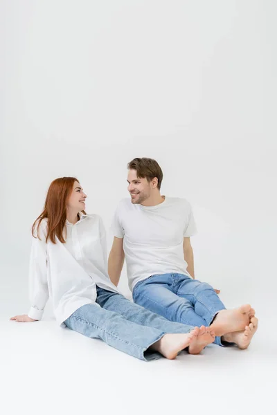 Positivo casal descalço olhando uns para os outros no fundo branco — Fotografia de Stock