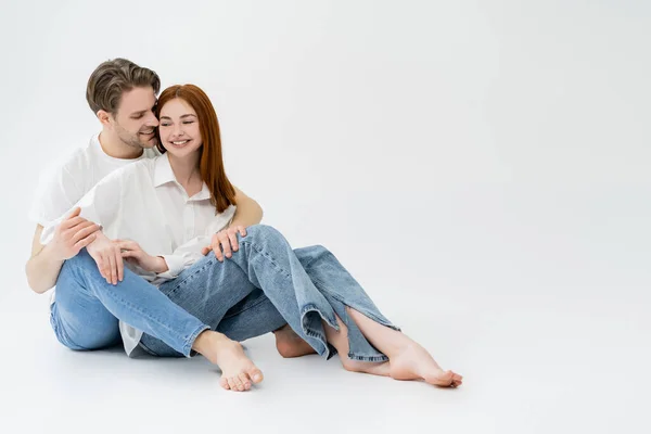 Uomo sorridente in jeans baciare fidanzata in camicia su sfondo bianco — Foto stock