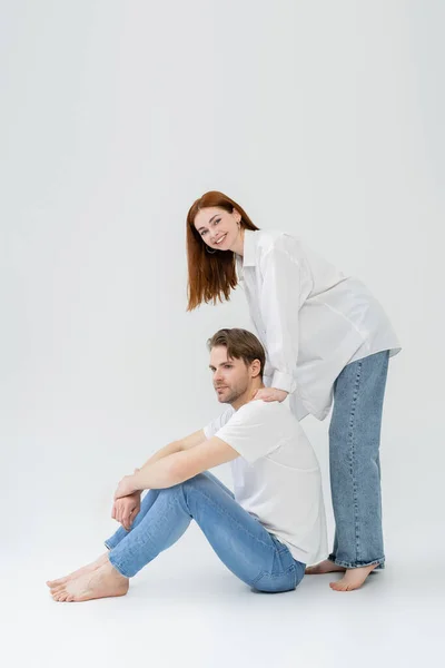 Smiling woman looking at camera while standing near boyfriend on white background — Stock Photo
