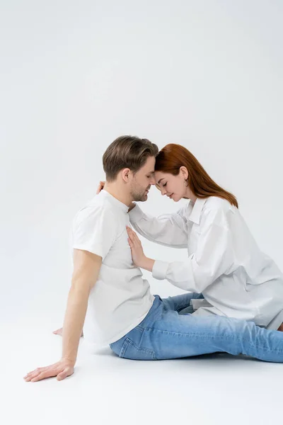 Side view of redhead woman with closed eyes touching chest of boyfriend on white background — Stock Photo