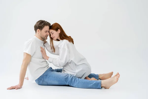 Vista laterale di giovane donna in camicia toccare fidanzato con gli occhi chiusi su sfondo bianco — Foto stock