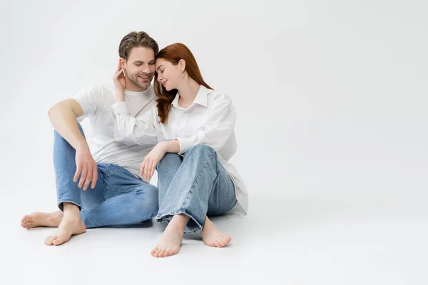 Barefoot woman touching ear of smiling boyfriend on white background — Stock Photo