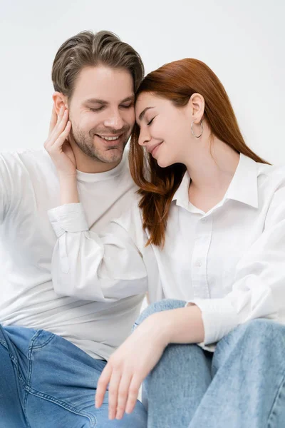 Mujer joven en camisa tocando sonriente novio aislado en blanco - foto de stock
