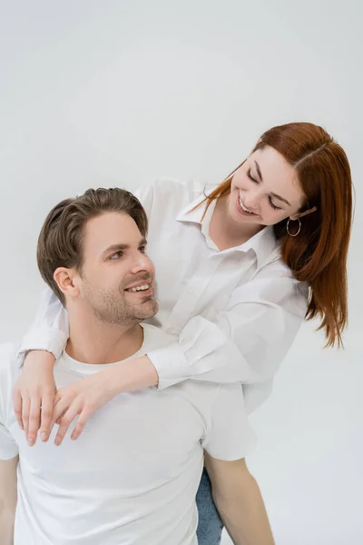 Mulher ruiva na camisa abraçando namorado positivo isolado no branco — Fotografia de Stock
