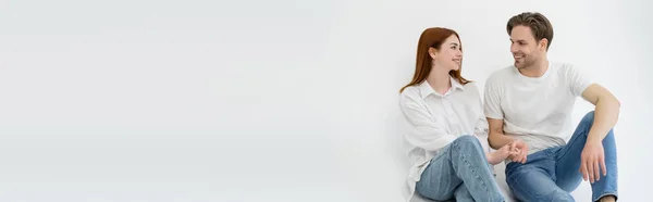 Positif jeune couple tenant la main tout en étant assis sur fond blanc, bannière — Photo de stock
