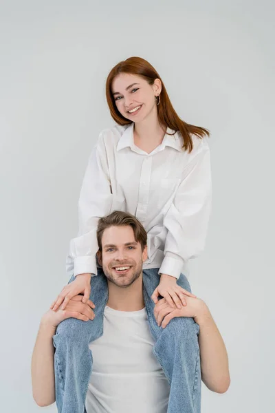 Mujer positiva sentada sobre hombros de novio aislado sobre blanco - foto de stock