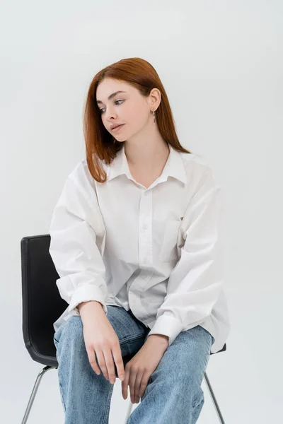 Молода жінка в сорочці сидить на стільці ізольовано на білому — стокове фото