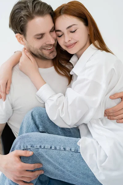 Uomo sorridente abbracciando fidanzata in jeans e camicia isolato su bianco — Foto stock