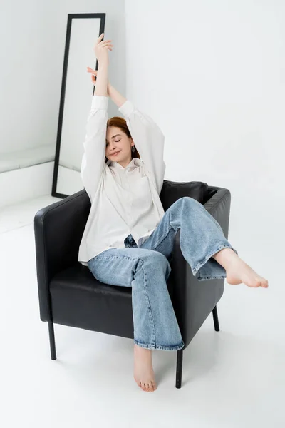 Mulher muito descalça sentada em poltrona no fundo branco — Fotografia de Stock
