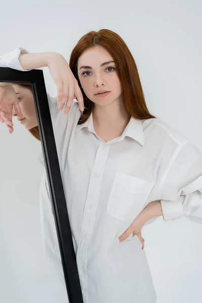 Красива молода жінка в сорочці позує біля дзеркала ізольована на білому — стокове фото