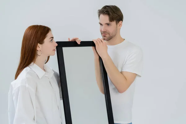 Giovane rossa donna guardando fidanzato vicino specchio isolato su bianco — Foto stock