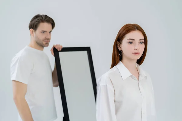 Junge rothaarige Frau steht neben verschwommenem Freund und Spiegel isoliert auf weißem Grund — Stockfoto