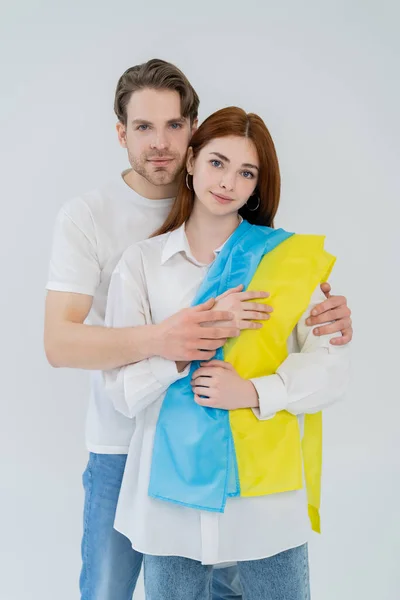 Jeune couple avec drapeau ukrainien regardant la caméra isolée sur blanc — Photo de stock