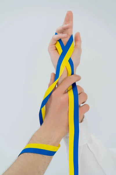 Обрізаний вид синьо-жовтої стрічки на руках молодої пари ізольовано на білому — стокове фото