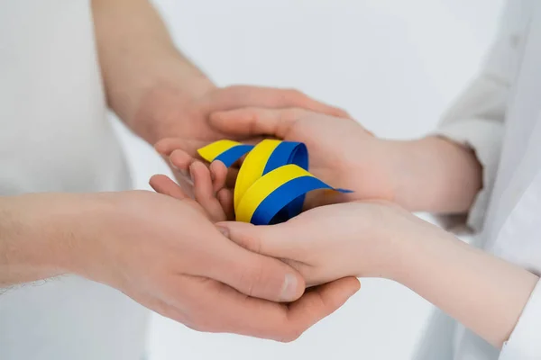 Vue recadrée du couple tenant la main et du ruban bleu et jaune isolé sur blanc — Photo de stock