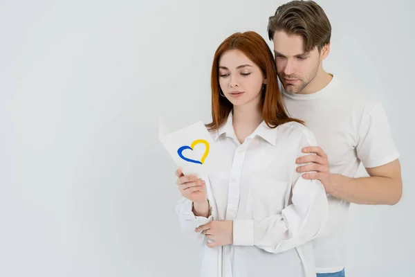 Man hugging girlfriend with blue and yellow heart sign isolated on white — Stock Photo