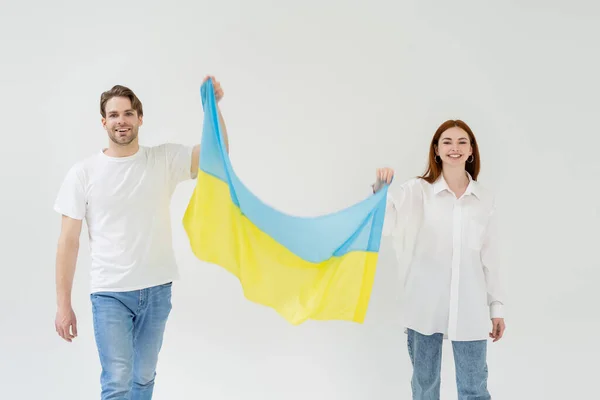 Alegre joven pareja sosteniendo bandera ucraniana aislada en blanco - foto de stock