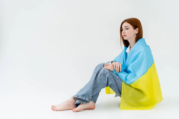 Barefoot woman in ukrainian flag sitting on white background — Stock Photo