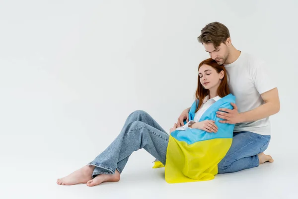 Young man hugging barefoot girlfriend in ukrainian flag on white background — Stock Photo