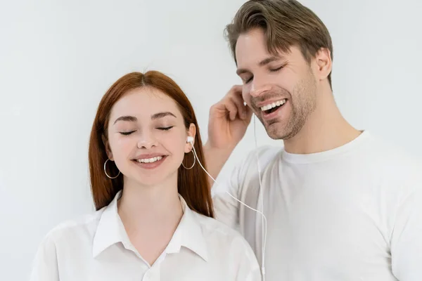 Cheerful young couple listening music in earphones isolated on white — Stock Photo