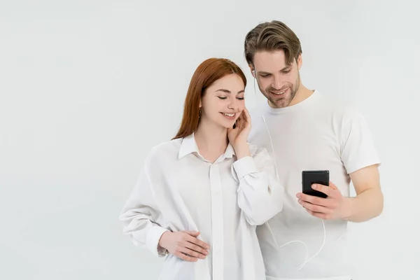 Casal alegre usando celular e fones de ouvido isolados no branco — Fotografia de Stock