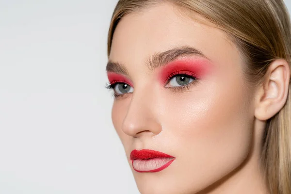 Mujer joven con sombra de ojos rojos mirando hacia otro lado aislado en gris - foto de stock