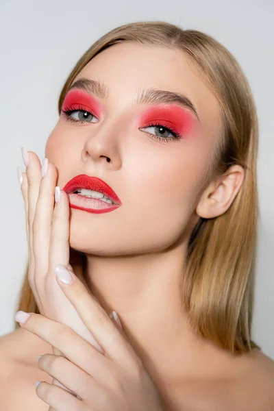 Modelo joven con maquillaje rojo mirando a la cámara aislada en gris - foto de stock