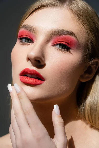 Retrato de mujer con labios rojos tocando barbilla aislada en gris - foto de stock