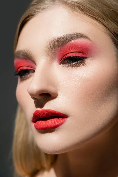 Nahaufnahme einer jungen Frau mit rotem Make-up, die isoliert von grau wegschaut — Stockfoto