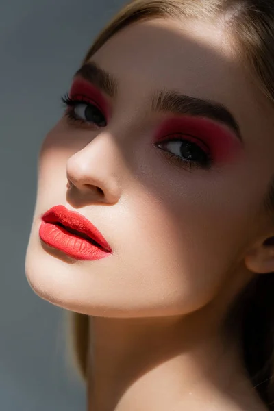 Young woman with red visage standing in shadow isolated on grey — Stock Photo