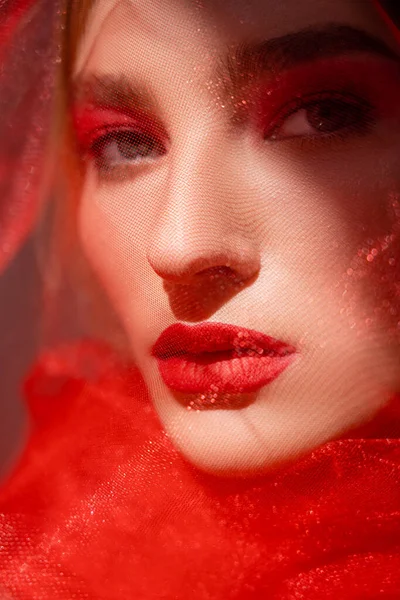 Jeune femme avec des lèvres rouges regardant la caméra près de tissu de tulle sur fond gris — Photo de stock