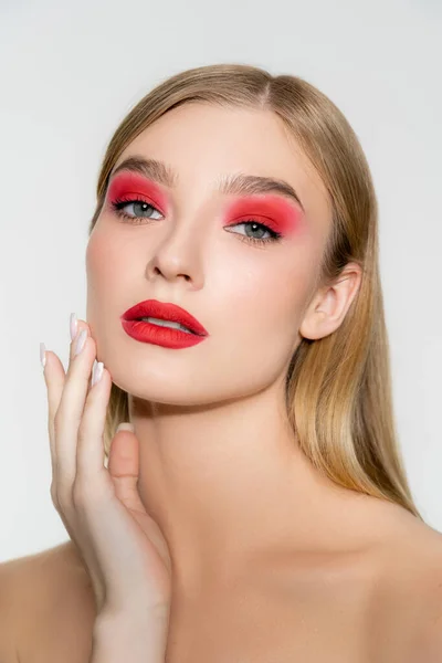 Modelo con hombros desnudos y maquillaje rojo tocando la cara aislado en gris - foto de stock