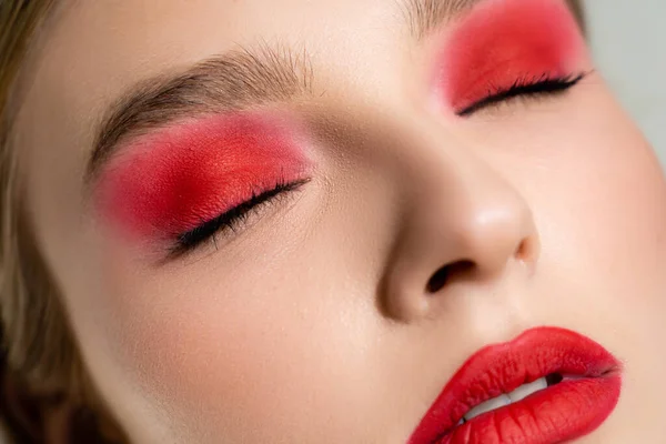 Vista de cerca de la mujer con los ojos de cierre de maquillaje rojo aislado en gris - foto de stock