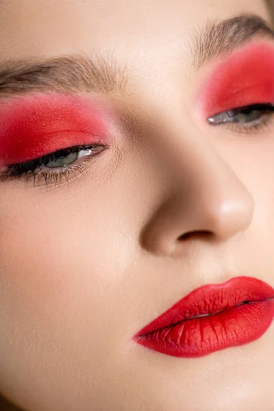 Close up view of young woman with red eye shadow and lips looking away — стоковое фото