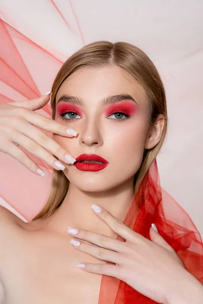 Jeune modèle avec lèvres rouges et ombre à paupières posant avec tissu sur fond gris — Photo de stock