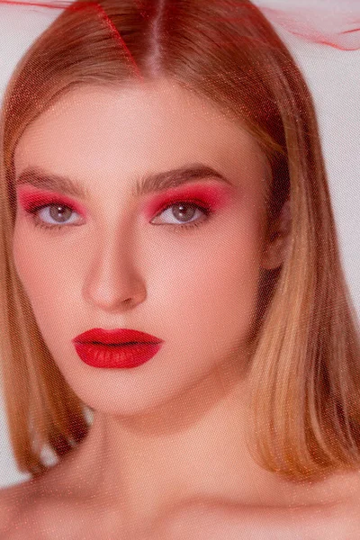 Portrait of fair haired model with red visage looking at camera near fabric on grey background — Stock Photo