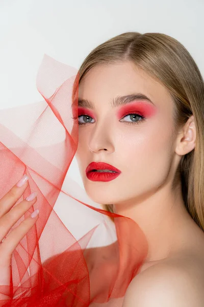 Jolie femme blonde aux épaules nues et aux lèvres rouges tenant un tissu en tulle isolé sur gris — Photo de stock