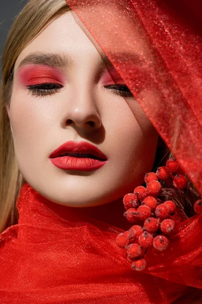 Портрет красивой модели с красным визажем, позирующим возле ткани и ягод, изолированных на сером — стоковое фото