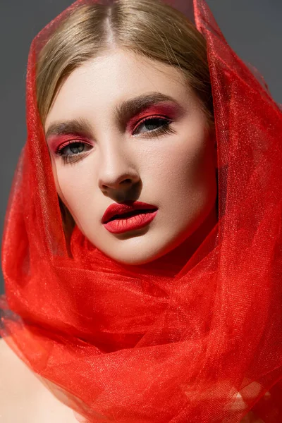 Retrato de modelo con rostro rojo y tela de tul mirando a la cámara aislada en gris - foto de stock