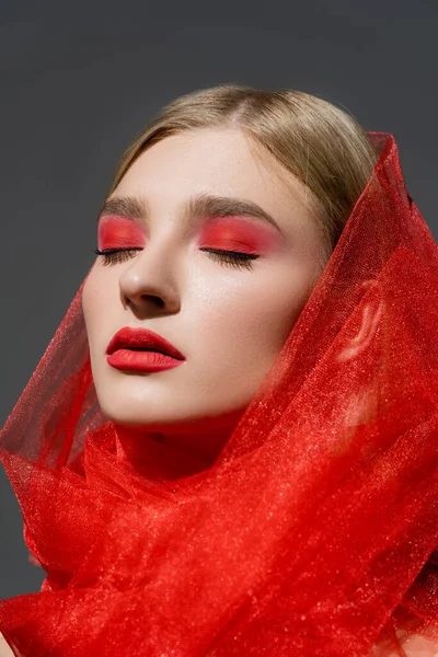 Young model with red eye shadow and cloth closing eyes isolated on grey — стоковое фото