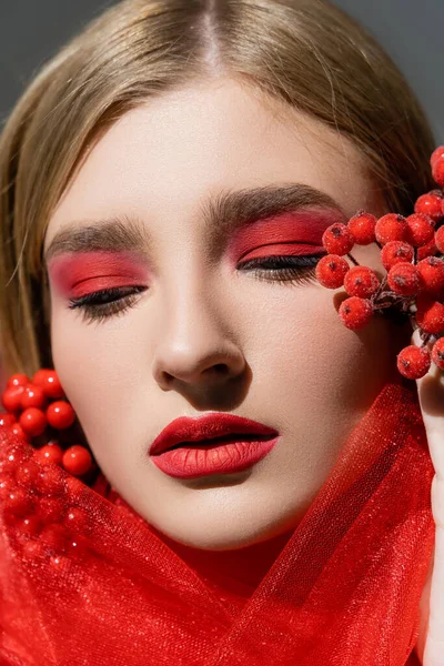 Retrato de modelo bonito con rostro rojo posando cerca de tela y bayas aisladas en gris - foto de stock