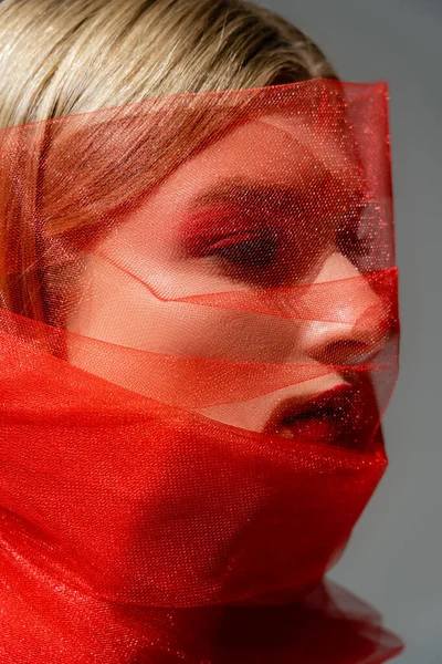 Schönhaariges Model in rotem Tülltuch schaut vereinzelt auf grauem Grund weg — Stockfoto