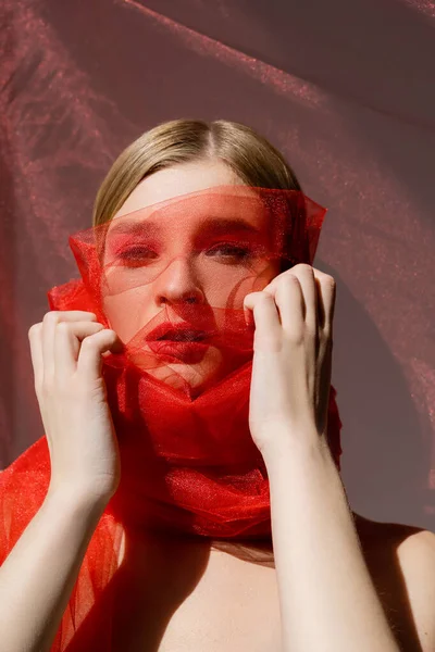 Jeune modèle avec lèvres rouges touchant tissu tulle sur fond gris — Photo de stock