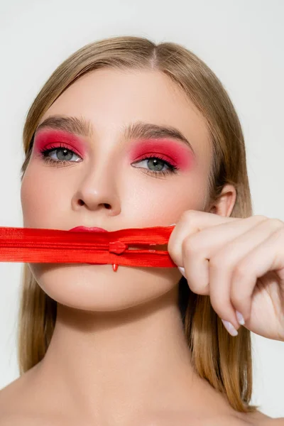 Mujer joven con sombra de ojos rojos sosteniendo cremallera aislada en blanco - foto de stock