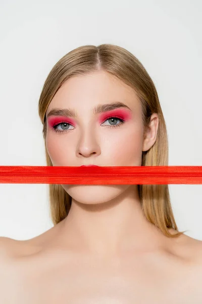 Woman with naked shoulders and red eye shadow holding zipper isolated on white — Stock Photo